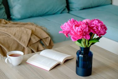 Üzerinde şakayık çiçekleri olan mavi cam vazo ve tahta masa üzerinde boş sayfalar ve arka planda mavi tekstil kanepe olan bir defter yakın çekim. Basit bir iç tasarım. Metin için alanı kopyala.