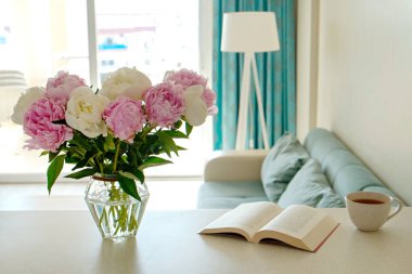 Ön planda cam vazoda beyaz şakayık çiçekleri ve arka planda mavi tekstil kanepe olan beyaz tezgahı yakından çek. Metin için boşluk kopyala, kapat.