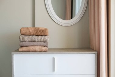 Yatak odasındaki şifoniyerin üstünde temiz, yeni yıkanmış, düzgünce katlanmış kadın kıyafetleri var. Pastel renkli süveter yığını. Boşluğu kopyala, kapat, arkaplan.