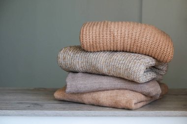 Yatak odasındaki şifoniyerin üstünde temiz, yeni yıkanmış, düzgünce katlanmış kadın kıyafetleri var. Pastel renkli süveter yığını. Boşluğu kopyala, kapat, arkaplan.