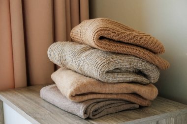 Yatak odasındaki şifoniyerin üstünde temiz, yeni yıkanmış, düzgün katlanmış giysiler yığını. Pastel renkli süveter yığını. Boşluğu kopyala, kapat, arkaplan.