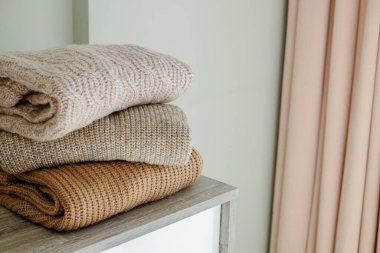 Yatak odasındaki şifoniyerin üstünde temiz, yeni yıkanmış, düzgün katlanmış giysiler yığını. Pastel renkli süveter yığını. Boşluğu kopyala, kapat, arkaplan.