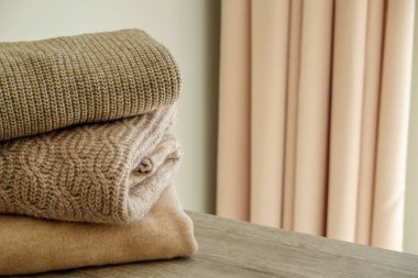 Yatak odasındaki şifoniyerin üstünde temiz, yeni yıkanmış, düzgün katlanmış giysiler yığını. Pastel renkli süveter yığını. Boşluğu kopyala, kapat, arkaplan.