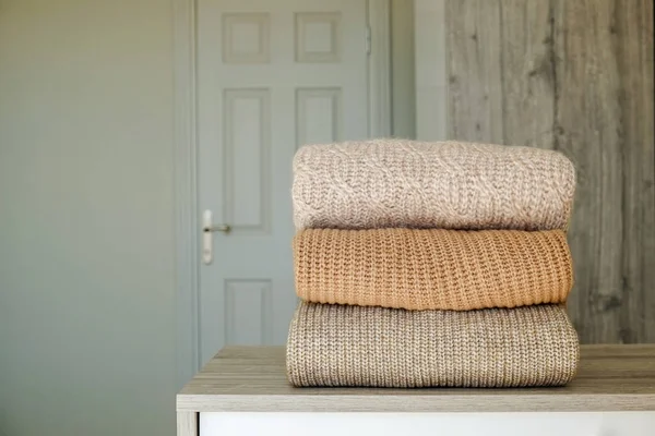 Stack of clean freshly laundered, neatly folded clothes on bedroom dresser\'s top. Pile of different sweaters of pastel colors. Copy space, close up, background.