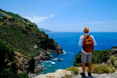 Fötr şapkalı ve sırt çantalı tipik bir turist mavi göl manzaralı, turkuaz suyla besleniyor. Akdeniz kıyısındaki bir uçurumda duran bir erkek yolcu. Boşluğu kopyala, arkaplan.