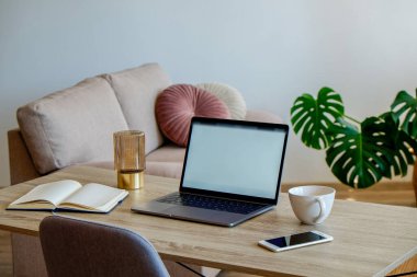 Boş ekran laptop, cep telefonu ve ahşap masada bir fincan. Doğal güneş ışığıyla dolu dekoratif palmiye bitkileriyle dolu rahat bir ofis. Kapat, kopyala boşluk, arkaplan.