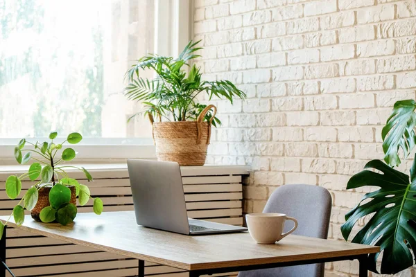 Creative workspace of a blogger. Laptop computer on wooden table in loft style corner office with brick walls and big windows. Designer\'s table concept. Close up, copy space, background.