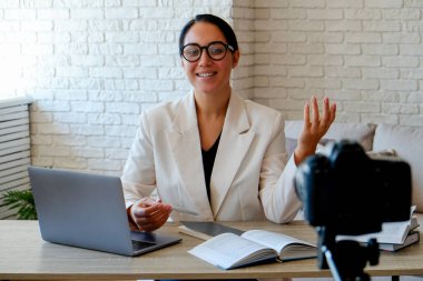 Çevrimiçi eğitim kavramı. Gözlük takan kadın öğretmen laptop ile ders veriyor, evinden canlı yayın yapıyor. Genç, güzel, zeki bir kadın konferans görüşmesinde..