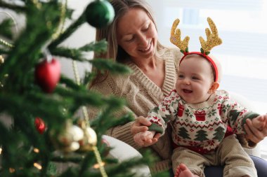 Anne bebeğiyle Noel ağacının yanında geyik boynuzu takıyor..