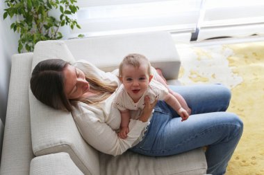 Genç anne kanepede neşeli bir bebek tutuyor. Boşluğu kopyala, arkaplan.