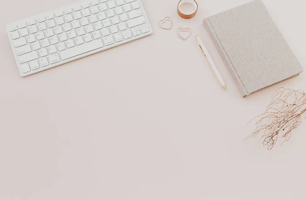 Klavyeli şık, minimalist bir iş yeri, pastel pembe arka planlı bir defter. düz yatış, üst görünüm
