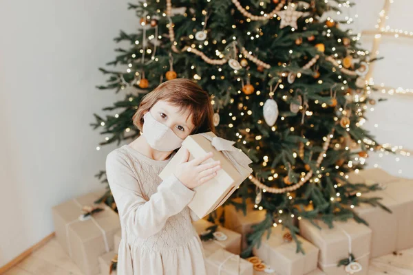 女孩在Covid 19大流行病中遇见了圣诞节 戴着防护口罩的孩子带着圣诞礼物 隔离社会距离 2021年新年假期 — 图库照片