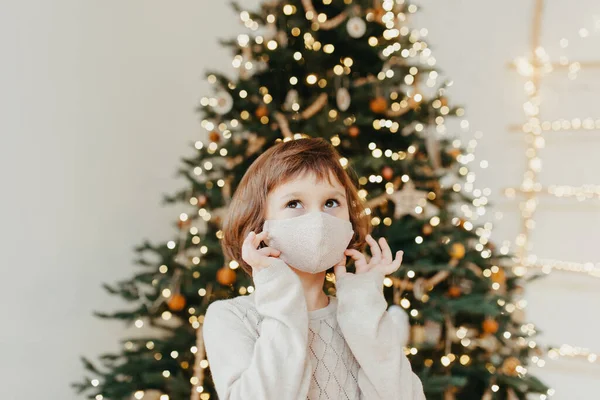 girl meets Christmas in the covid-19 pandemic. Child in a protective medical mask. Quarantine isolation social distance. New year holidays 2021. Kid in Face cover