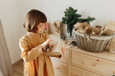 Çocuklar için Noel takvimi. Hardal keten elbise giyen bir kız hediye paketi tutuyor. Çevre dostu Noel.