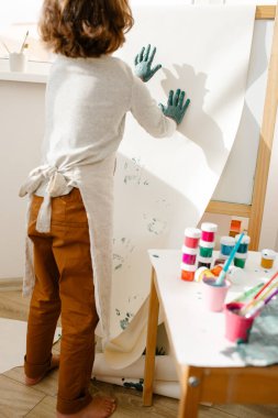 Çocuk kız elini boya ve fırçayla boyuyor. Çocuklar için parmak boyama ya da sanat terapisi. Yürümeye başlayan çocuklar için eğlenceli aktiviteler.