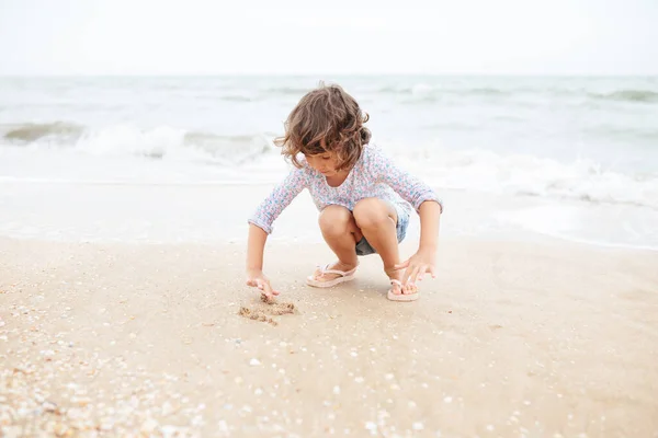 Cinco años lindo rizado caucásico chica pintura en arena en la playa. —  Fotos de Stock