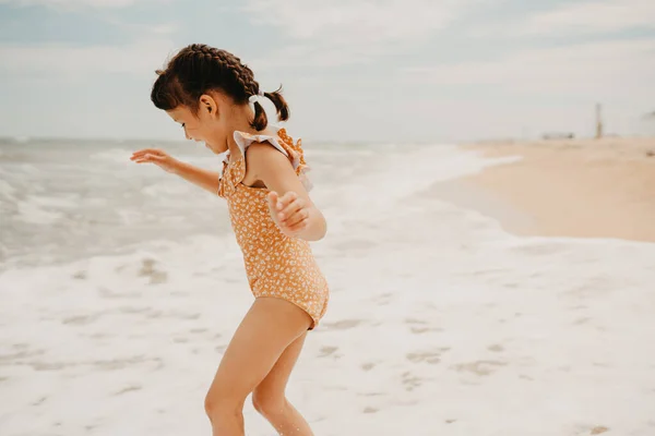 Niña de seis años en traje de baño amarillo en la playa, gente por detrás. —  Fotos de Stock