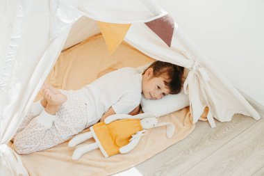 Güzel bir kız çadırda kumaş tilda tavşanla oynuyor.