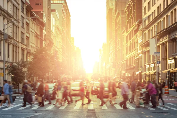 People walking across a busy intersection with the bright light of sunset in the background - Manhattan, New York City NYC