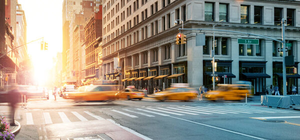 New York City - Busy intersection with yellow taxis speeding through the crowded intersection of 5th Avenue and 23rd Street with the light of sunset shining in the background
