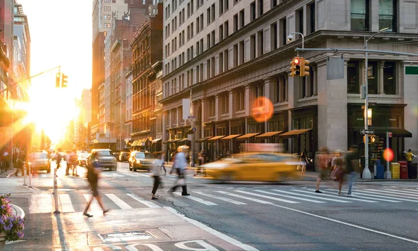 Busy New York City scene with crowds of people and cars in the intersection of Fifth Avenue and 23rd Street in Midtown Manhattan with the light of sunset in the background