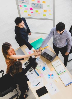 Dört iş adamından oluşan bir grup masanın etrafında çalışıyor ve ellerini birleştiriyor. Takım çalışması ve birlik hedefi vaatlerini sergiliyorlar..