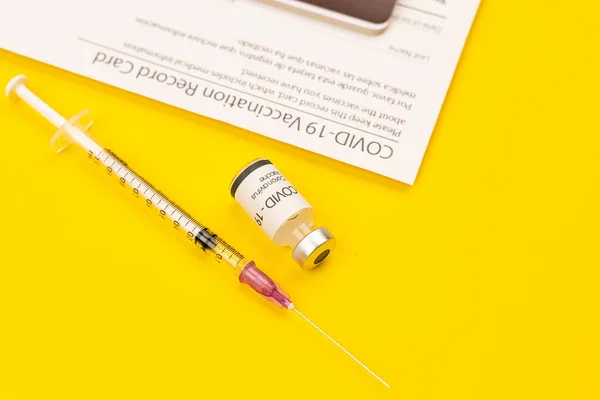 Covid 19コロナウイルスワクチンと注射器のボトルは黄色の背景に置かれ コピースペースが付いている記録カードをワクチン接種した ウイルス感染症の治療法の普及のための概念 — ストック写真