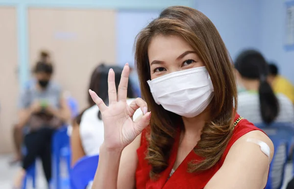 Asian woman wearing medical hygiene face mask showing finger in OK sign with happy and safe after getting vaccine for coronavirus or Covid-19.