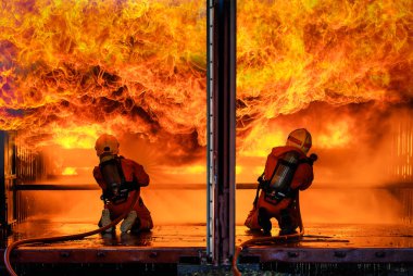 İki itfaiye ekibi, oksijen tüplü üniforma giyip su dökerek dar felaket bölgesinde cesur ve sorumluluk sahibi iki büyük turuncu ateşe göğüs gerdiler..