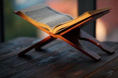 Kuran-ı İslami kutsal kitap. Geleneksel Müslüman tarzı ahşap duruş. Turuncu güneş ışığı ve yeşil ağaç arkaplanı fotokopi alanı ile bulanık..