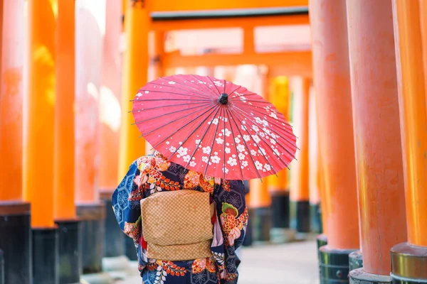 京都の伏見稲荷神社にある赤い木製の鳥居の中に日本の着物を着た芸者の女の子 着物は日本の伝統的な服です 着物という言葉は 実際には 着るもの を意味します — ストック写真