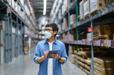 Yeni normal Asyalı adamlar, personel, yüz maskesi takan ürünler. Depo Kontrol Müdürü 'nü de sayarsak depodaki ürünleri sayıyor ve denetliyor.