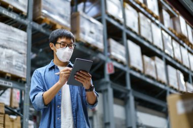 Yeni normal Asyalı adamlar, personel, yüz maskesi takan ürünler. Depo Kontrol Müdürü 'nü de sayarsak depodaki ürünleri sayıyor ve denetliyor.