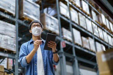 Yeni normal Asyalı adamlar, personel, yüz maskesi takan ürünler. Depo Kontrol Müdürü 'nü de sayarsak depodaki ürünleri sayıyor ve denetliyor.