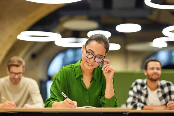 Never stop learning. Focused asian woman wearing eyeglasses making some notes while studying with colleagues during corporate training or seminar