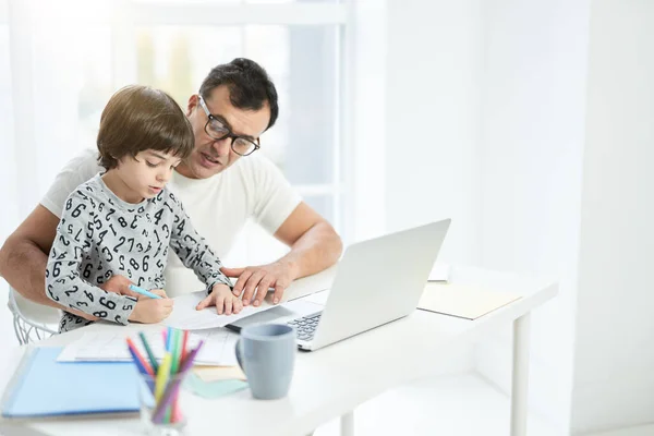 Help your child. Loving latin father playing with his son. Businessman using laptop while working from home and watching child