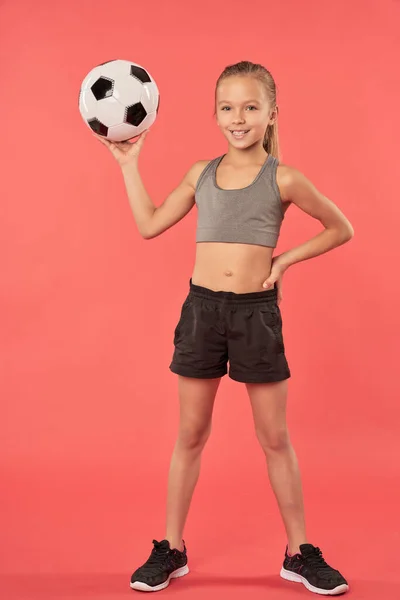 Cute female child with soccer ball standing against red background