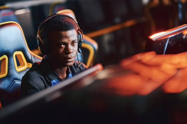 Young african guy, male professional cybersport gamer wearing headphones looking at camera while playing online video game