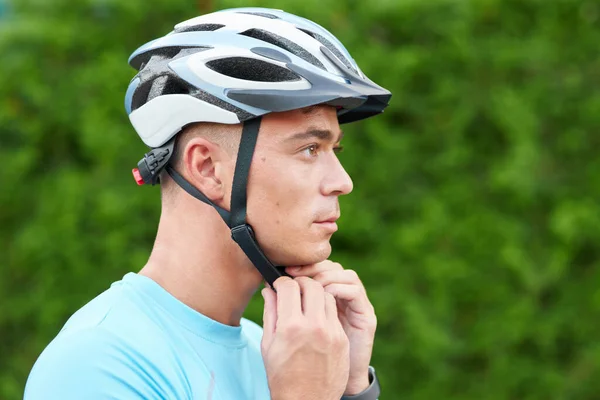 Get ready. Portrait of handsome male cyclist putting helmet on his head, getting ready, standing outdoors in nature