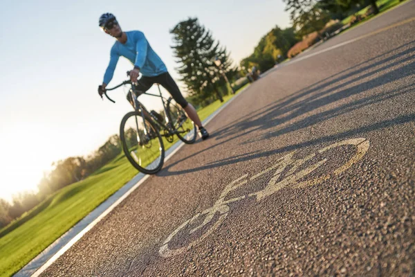 Close up of a bicycle sign drawn on asphalt. Professional male cyclist standing with his bike on a cycle path in the background