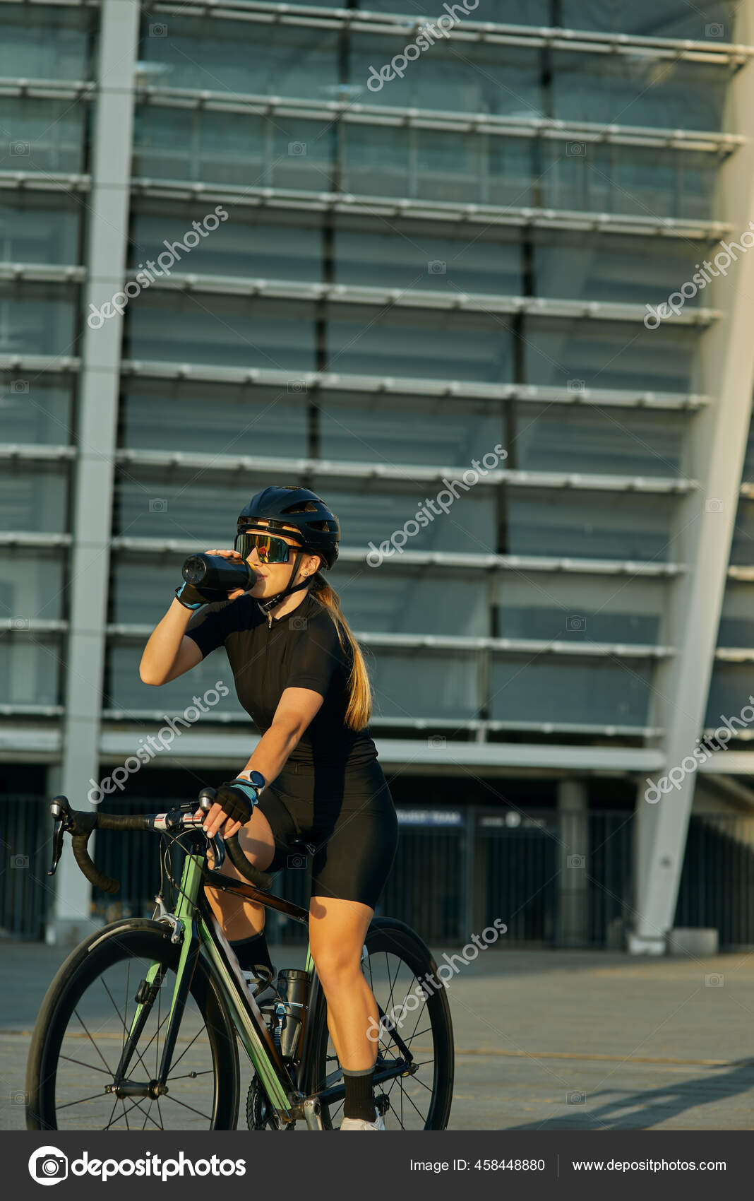 Ciclista profesional en ropa de ciclismo negro y equipo de protección de agua potable mientras en bicicleta en la ciudad, entrenando al aire libre en día cálido: de stock ©