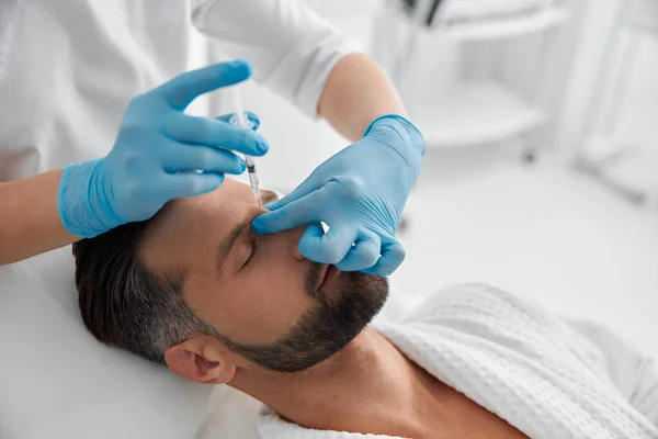Attractive middle aged man undergoes nasal bridge filler procedure in cosmetology clinic