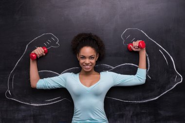Smiling afro-american woman with dumbbells and painted arms on chalkboard