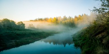 Sis ve güneş ışığıyla güzel bir nehir sabahı. Kuzey Avrupa 'daki nehir kıyılarının bahar manzarası. Sıcak, renkli görünüş.