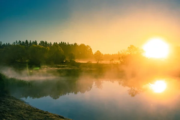 A beautiful spring landscape of a river valley with morning mist. Springtime scenery of a river flowing through the forest. Water evaporating in sun rays. Springtime scenery of Northern Europe.