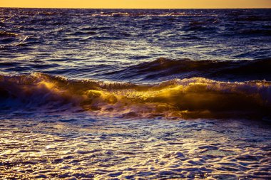 Kumlu sahile yakın dalgaların olduğu güzel bir gün batımı manzarası. Güneş su yüzeyinde parlıyor. Baltık Denizi 'nde renkli deniz manzarası.
