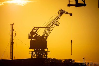 Limandaki batan güneş diskine karşı güzel metal vinç siluetleri. Riga, Letonya 'nın sanayi şehri.