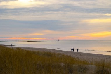 Güzel bir yaz günbatımı manzarası. Sahilde yürüyen siluetler, Baltık Denizi 'nin kostüm çizgisinin keyfini çıkarıyorlar. Letonya, Avrupa 'nın akşam manzarası.