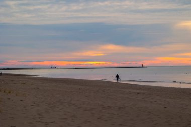 Güzel bir yaz günbatımı manzarası. Sahilde yürüyen siluetler, Baltık Denizi 'nin kostüm çizgisinin keyfini çıkarıyorlar. Letonya, Avrupa 'nın akşam manzarası.