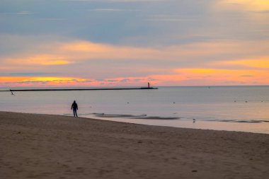 Güzel bir yaz günbatımı manzarası. Sahilde yürüyen siluetler, Baltık Denizi 'nin kostüm çizgisinin keyfini çıkarıyorlar. Letonya, Avrupa 'nın akşam manzarası.
